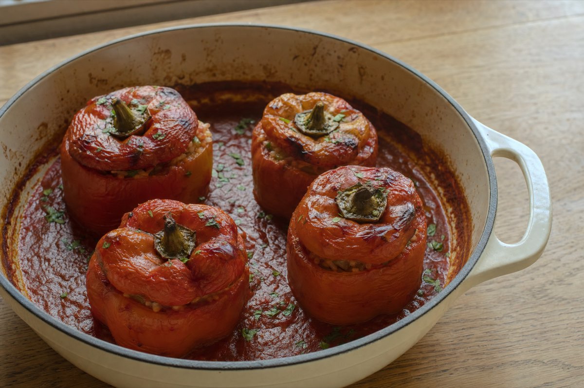 Vier gefüllte Paprika in Tomatensauce in einem breiten Topf