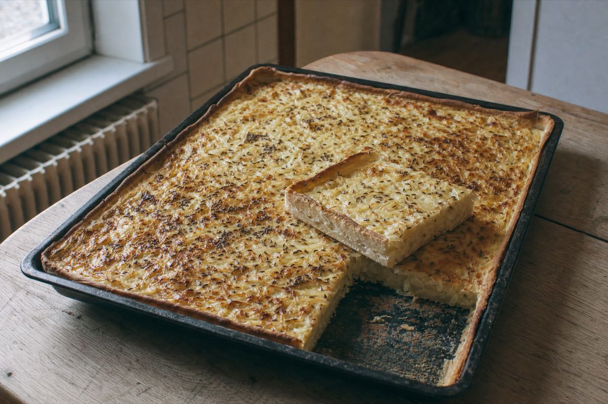 Zwiebelkuchen vom Blech mit goldbrauner Oberfläche und Kümmel, ein Stück ist herausgeschnitten